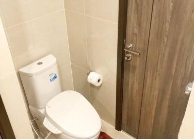 Modern bathroom interior with a clean toilet, beige tiles, and wooden door
