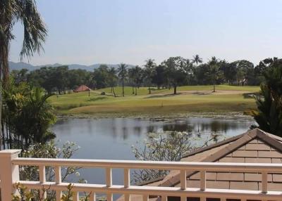 Balcony view of a golf course with pond and trees under clear sky