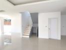 Spacious and bright unfurnished living space with staircase and glossy tiled flooring