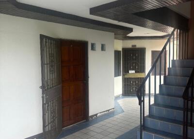 Covered front entrance of a residential building with a wooden door and staircase