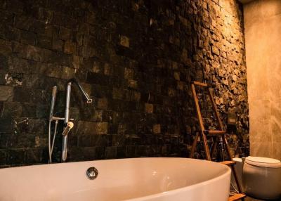 Elegant bathroom with a freestanding bathtub, textured black stone walls, and warm lighting