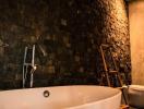 Elegant bathroom with a freestanding bathtub, textured black stone walls, and warm lighting