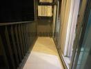 Compact balcony with metal railing and an external air conditioning unit at night