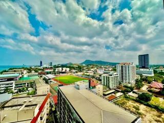 Panoramic view of a cityscape with buildings and a mountain in the background under a blue sky with clouds