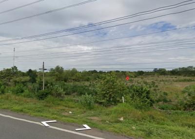 Empty land near a road with power lines and greenery under a cloudy sky