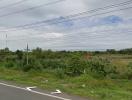 Empty land near a road with power lines and greenery under a cloudy sky