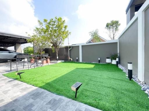 Spacious backyard with artificial grass, patio area, and a carport on a sunny day