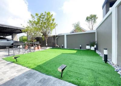 Spacious backyard with artificial grass, patio area, and a carport on a sunny day