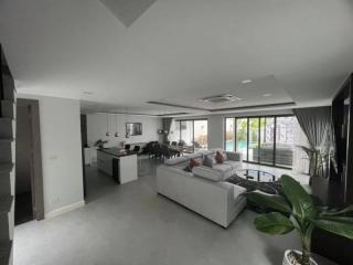 Spacious and modern living room with open floor plan connecting to kitchen and dining area, leading to an outdoor space