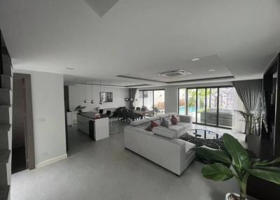 Spacious and modern living room with open floor plan connecting to kitchen and dining area, leading to an outdoor space