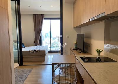 Modern studio apartment interior with an open bedroom, kitchenette, and large window