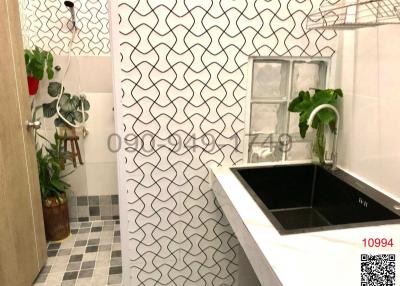 Modern bathroom with geometric tiled walls, black sink, and potted plant decor