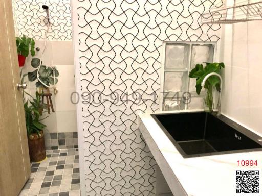 Modern bathroom with geometric tiled walls, black sink, and potted plant decor