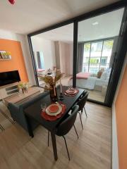 Modern dining area with an open layout towards the living space, featuring a black dining table, a large window, and hardwood flooring