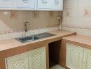 Compact kitchen with beige storage cabinets and stainless steel sink