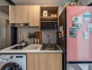 Modern compact kitchen with stainless steel appliances and pink refrigerator