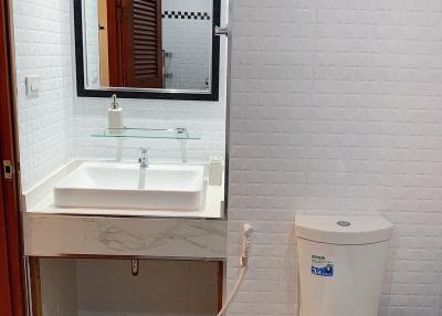 Modern bathroom with white tiling and fixtures, including sink, toilet, and mirror
