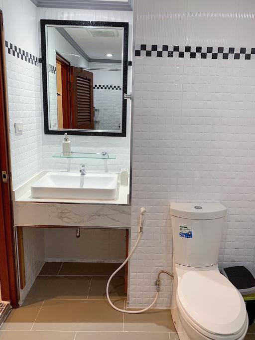 Modern bathroom with white tiling and fixtures, including sink, toilet, and mirror