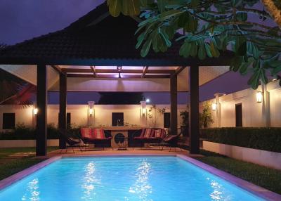 Illuminated outdoor swimming pool with lounge chairs and tropical trees during twilight