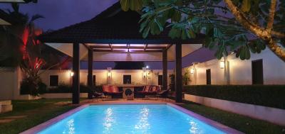 Illuminated outdoor swimming pool with lounge chairs and tropical trees during twilight