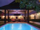 Illuminated outdoor swimming pool with lounge chairs and tropical trees during twilight