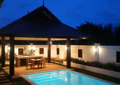 Well-lit private pool with covered dining area during evening
