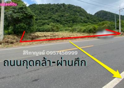 Paved road near a mountainous area with a land plot for sale indicated by arrows and contact information