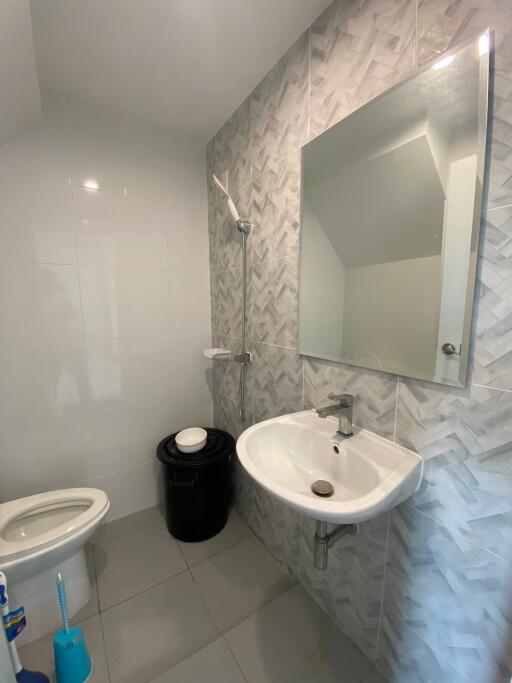 Modern bathroom with white and gray tiling, wall-mounted sink, and large mirror