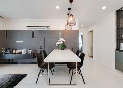 Spacious and modern open-concept living room with adjoining kitchen, featuring a large dining table, sleek cabinetry, and contemporary lighting fixtures