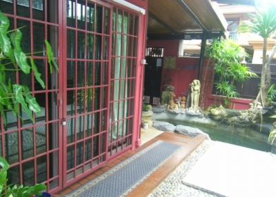 Cozy patio area with red metal security gates, stone pathway, and a serene pond