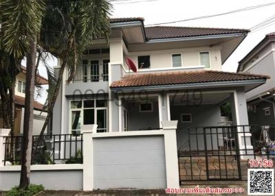 Modern two-story residential home with a balcony and carport, surrounded by a metal fence and palm trees