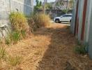 Narrow pathway leading to a car parked outside between concrete walls and metal fencing