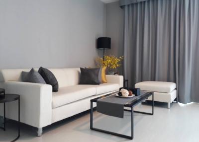 Modern living room with a white sofa, glass coffee table, and gray curtains