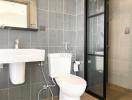 Modern bathroom with grey tiles, glass shower, and white fixtures