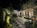 Well-lit exterior of a residential building at night with landscaped garden and tiled pathway