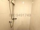 Compact bathroom shower area with white tiles and electric shower unit