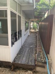 Narrow outdoor walkway beside a residential building with a wooden deck and fenced boundaries