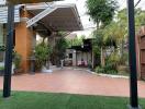 Spacious outdoor patio with a mix of tile and artificial grass, covered seating area, and surrounded by lush greenery