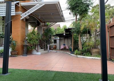 Spacious outdoor patio with a mix of tile and artificial grass, covered seating area, and surrounded by lush greenery