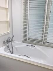 Modern white bathtub with stainless steel fixtures and closed window blinds