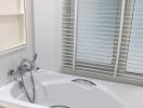 Modern white bathtub with stainless steel fixtures and closed window blinds