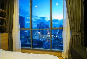 Modern bedroom with floor-to-ceiling window overlooking the city at dusk