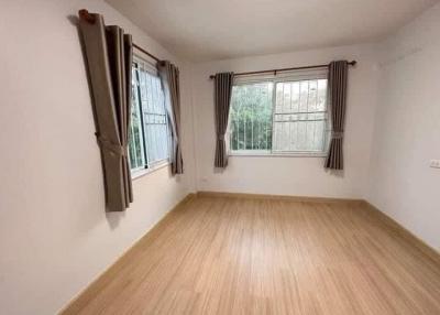 Empty bedroom with wooden flooring and two curtained windows