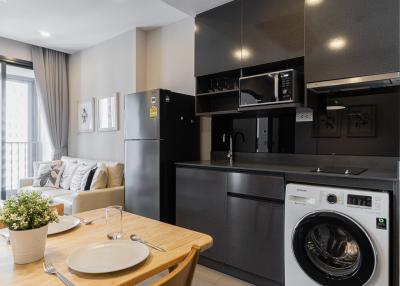 Modern kitchen with integrated appliances next to a cozy living space with sofa and balcony access