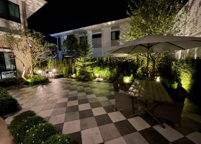 Spacious outdoor garden with illuminated landscaping and tiled patio at night