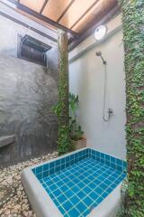 Outdoor bathroom with a blue-tiled soaking tub, shower, and greenery