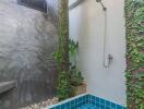 Outdoor bathroom with a blue-tiled soaking tub, shower, and greenery