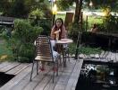 Woman sitting at a table in a scenic outdoor patio area by a pond