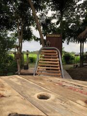 Wooden bridge leading to a rustic outdoor building surrounded by greenery