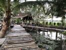 Rustic wooden walkway leading to a thatched hut by a pond with lush greenery